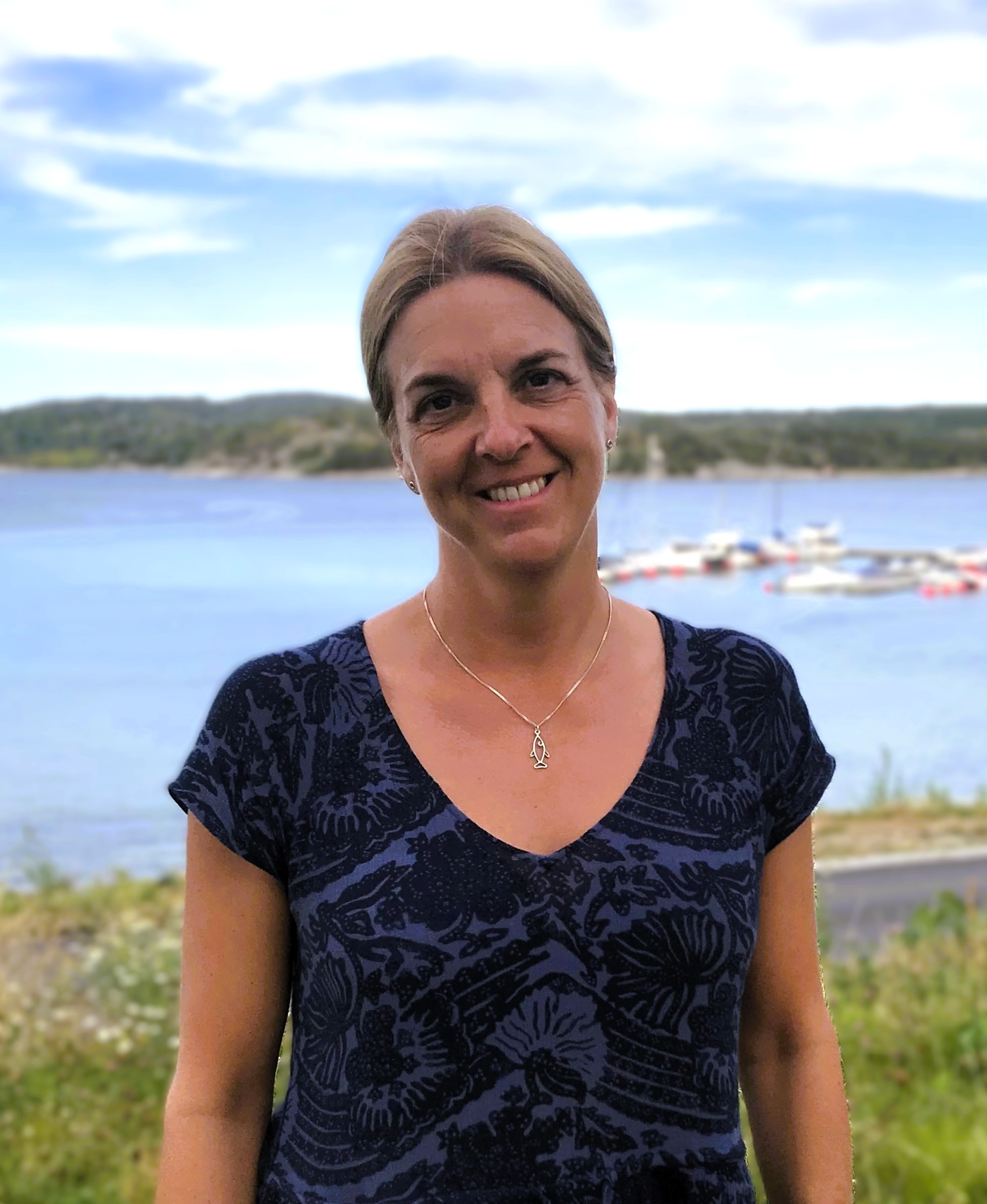 Bild på leende kvinna med havet som bakgrund.